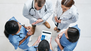 A group of healthcare providers discussing a patient's care plan while referencing electronic devices.